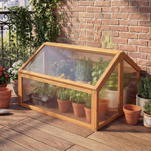 Load image into Gallery viewer, Wooden greenhouse with plants on a wooden deck against a brick wall.